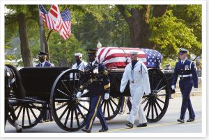 Horse-drawn hearse carrying coffin draped with American flag